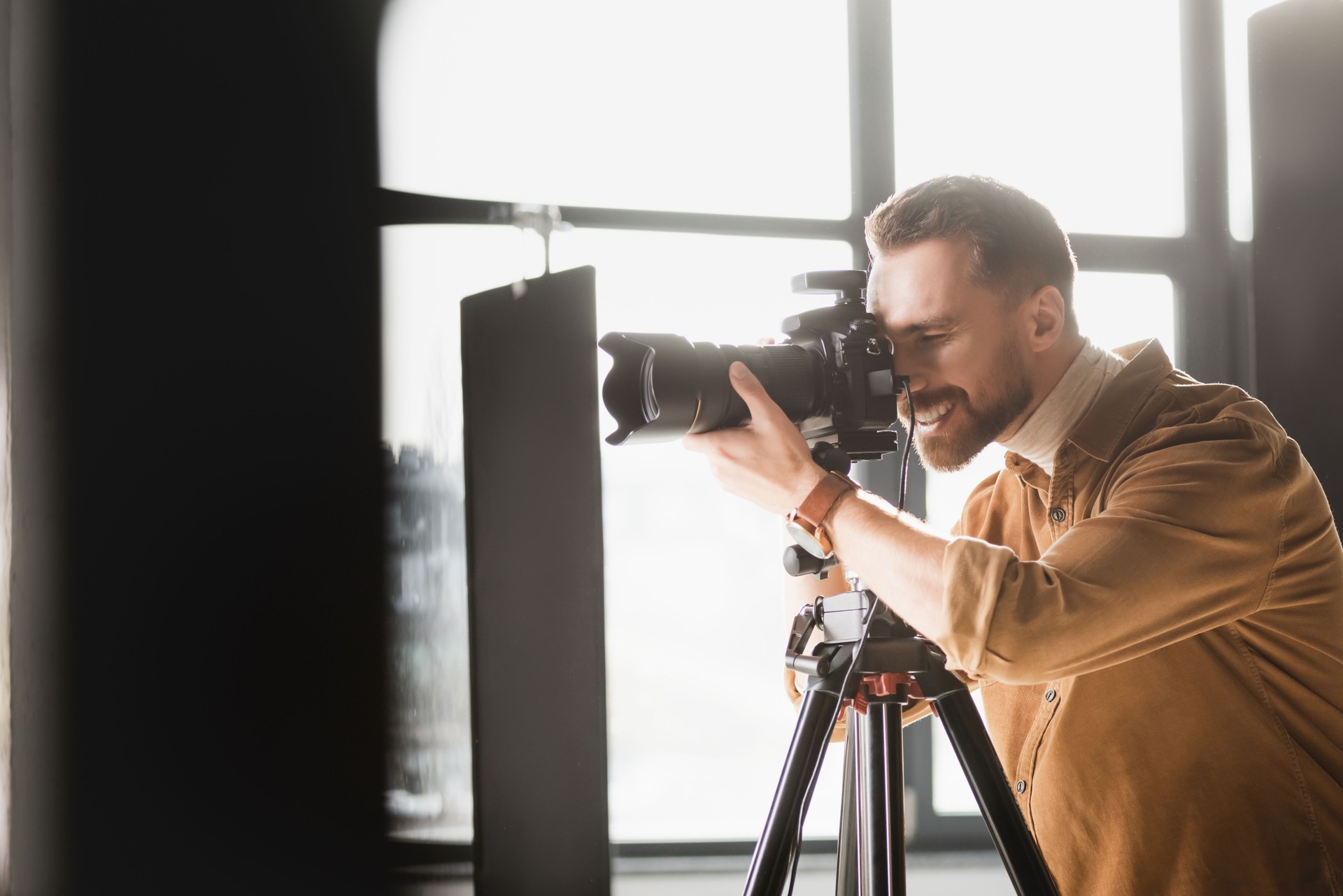 selective focus of smiling photographer taking photo with digital camera on backstage